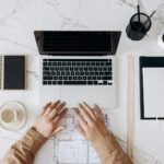 person in brown long sleeve shirt using macbook pro beside white ceramic mug